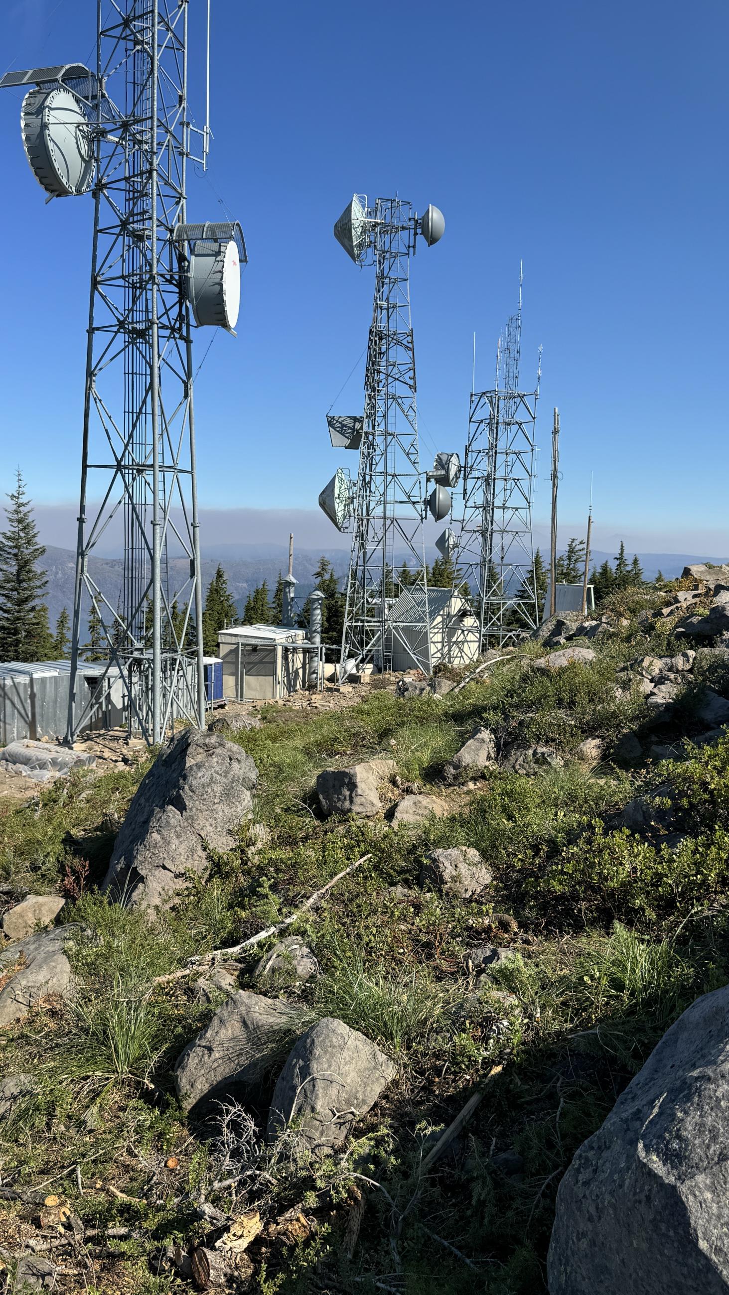 Communications towers with vegetation cleared around them and mountains in the background