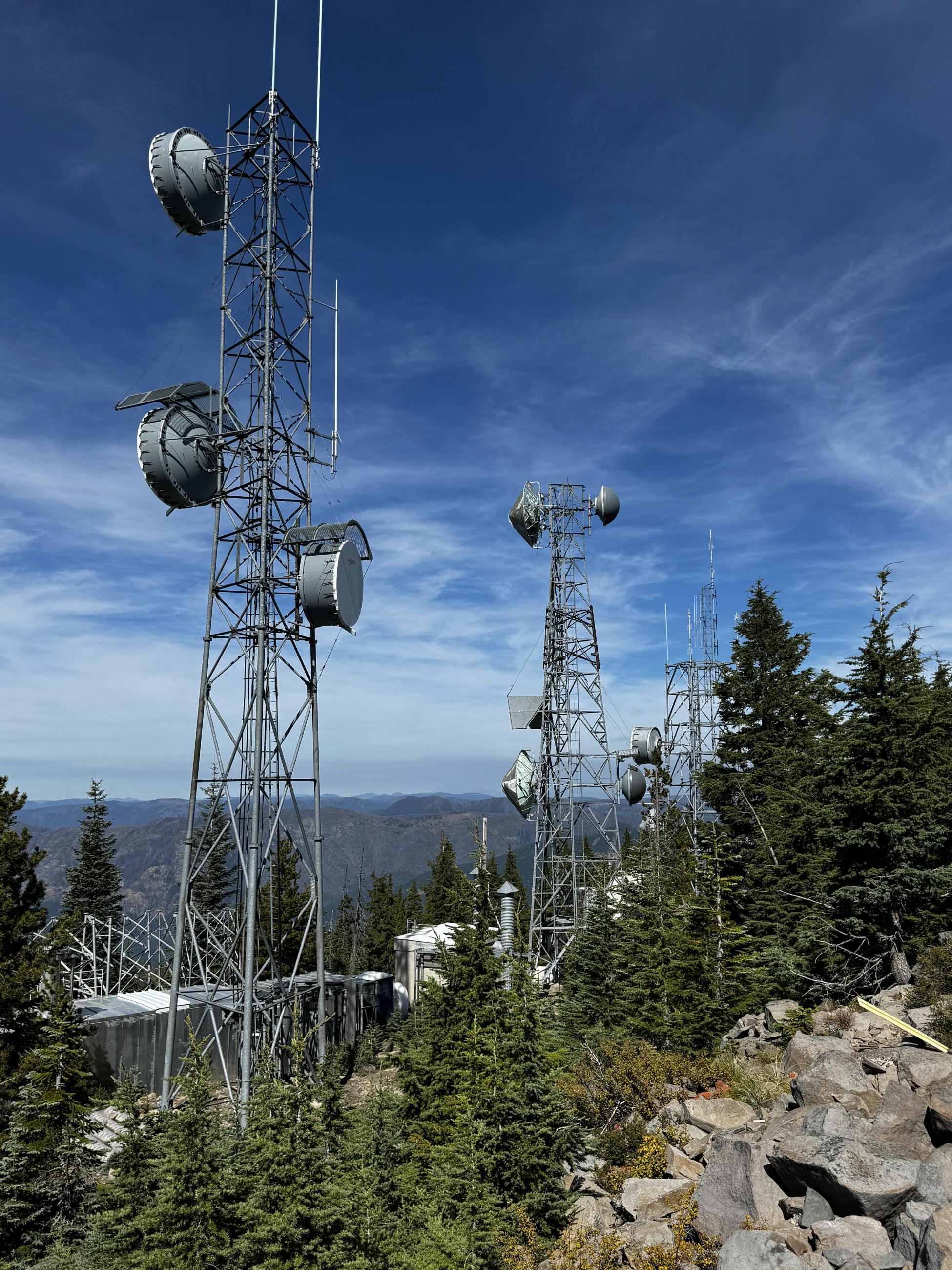 Communications towers on top of a mountain with forest in the background