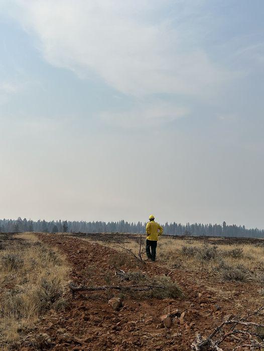 A Resource Advisor evaluates a dozer line with smoke in the background 