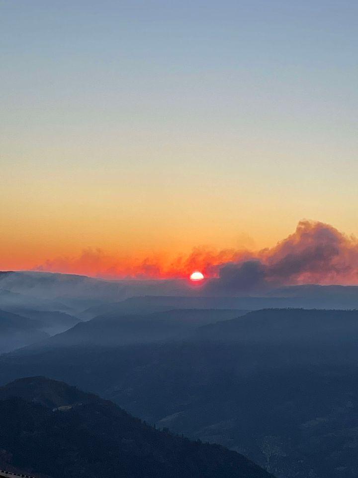 A view of sunset and smoke column from the Rail Ridge Fire with mountains in the foreground and smoke in the valleys below