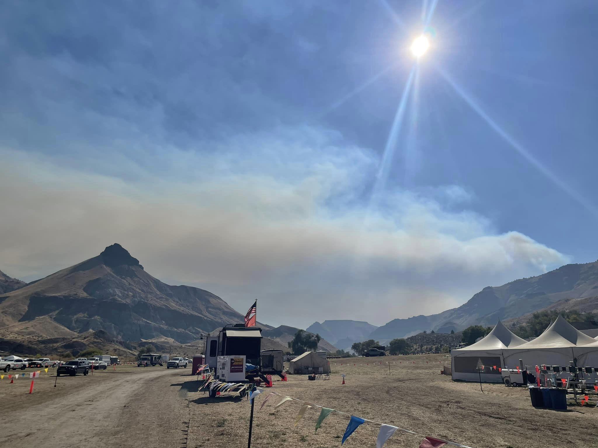 A large smoke column can be seen behind mountainous terrain and parts of the Dayville Incident Command Post