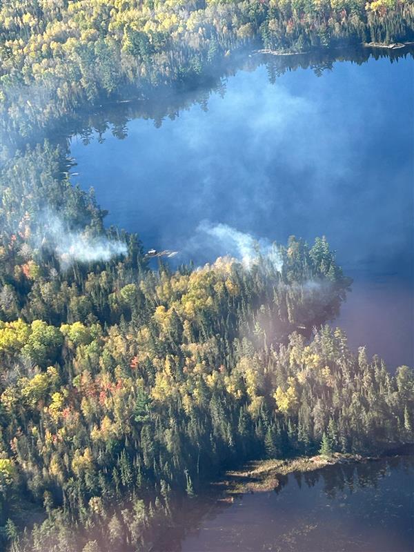 Aerial view of white smoke rising from the forest with Shell Lake on the top and left side