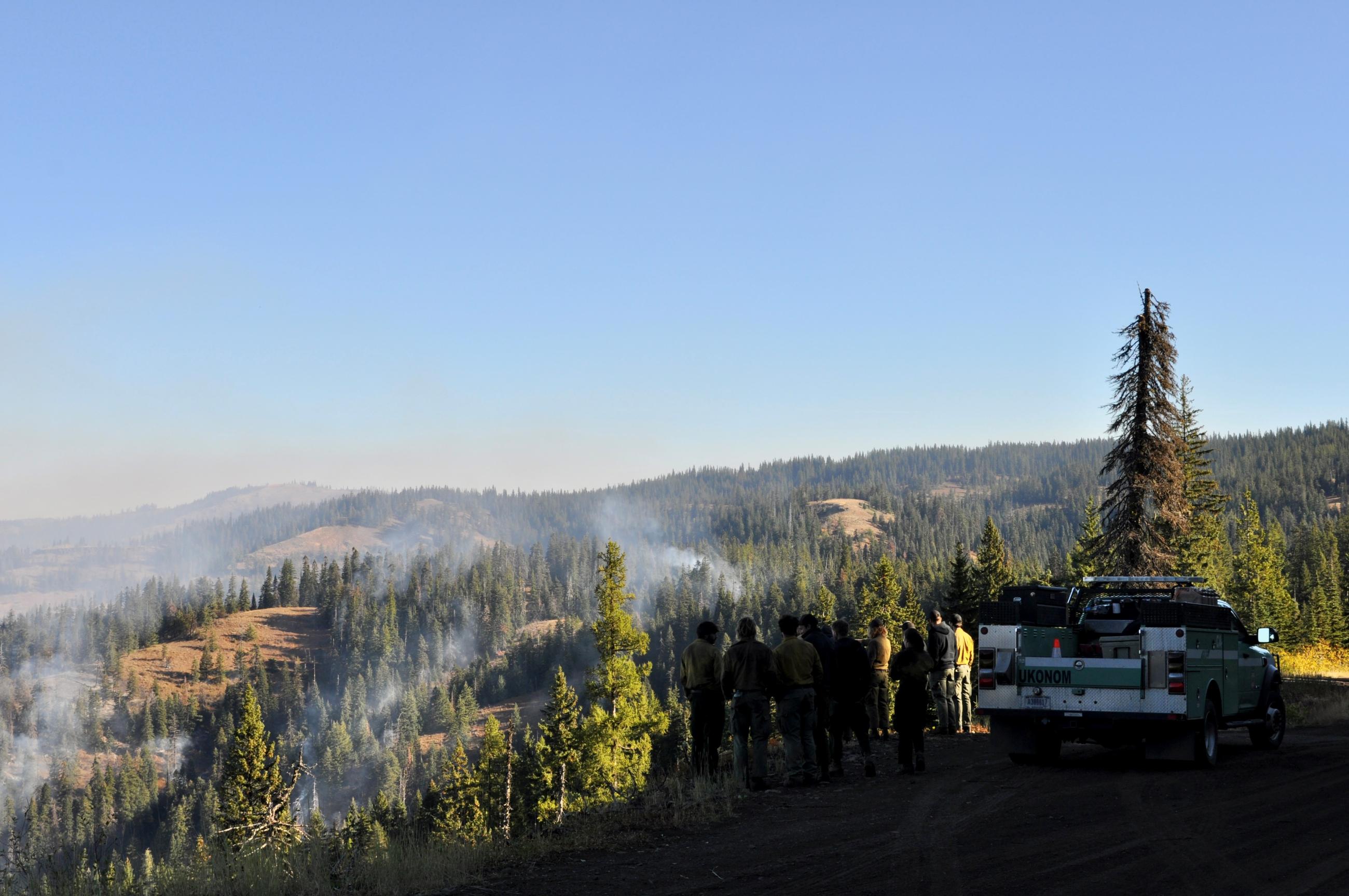 Group of firefighters stand at high ridge overlooking smoke from fire