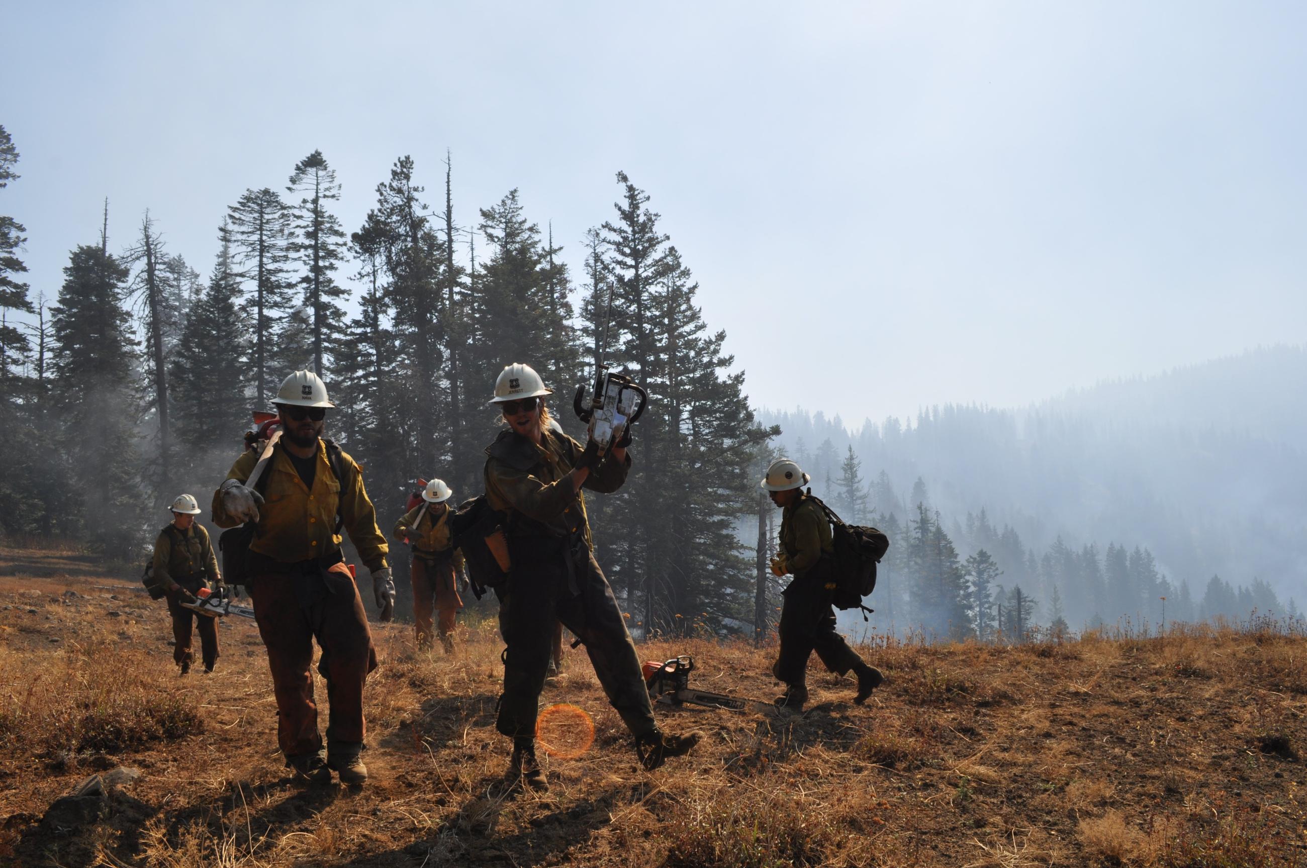 Group of firefighters chatting as they walk and carry tools