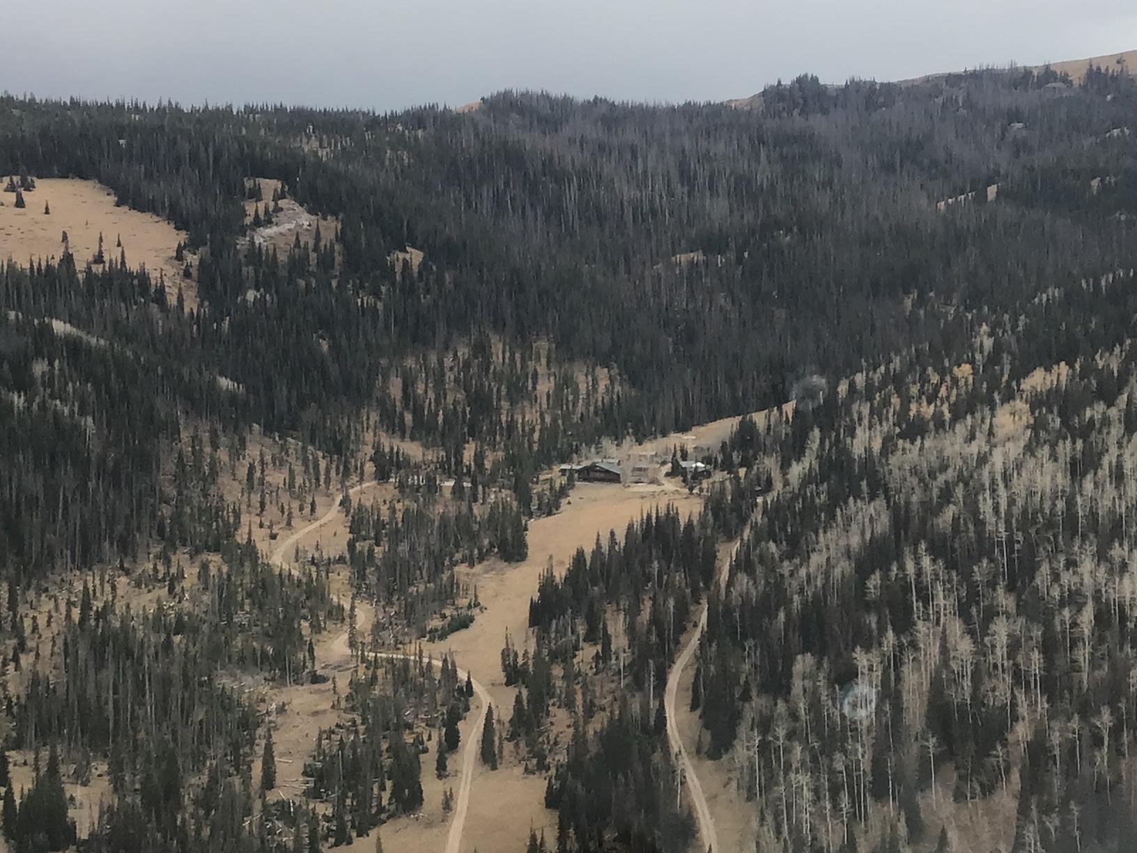 Overhead view of a camp nestled in the mountain valley with pine trees on the mountainside and a two track road through the center.