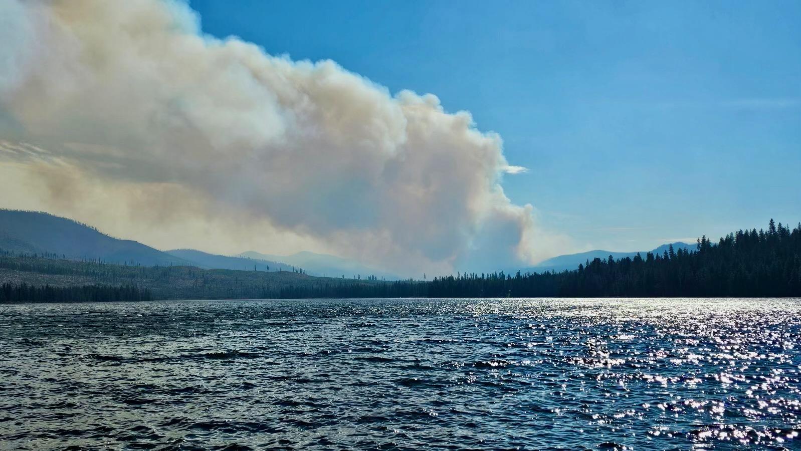 Warm Lake is in the foreground and a smoke column from the Goat Fire is seen in the distance on the afternoon of October 4, 2024.