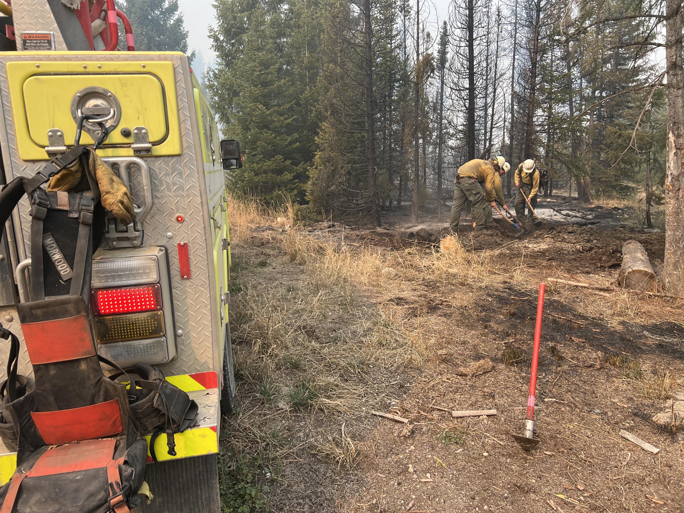 Part of a fire engine is seen at left and three firefighters use tools to extinguish a hot spot on October 5.