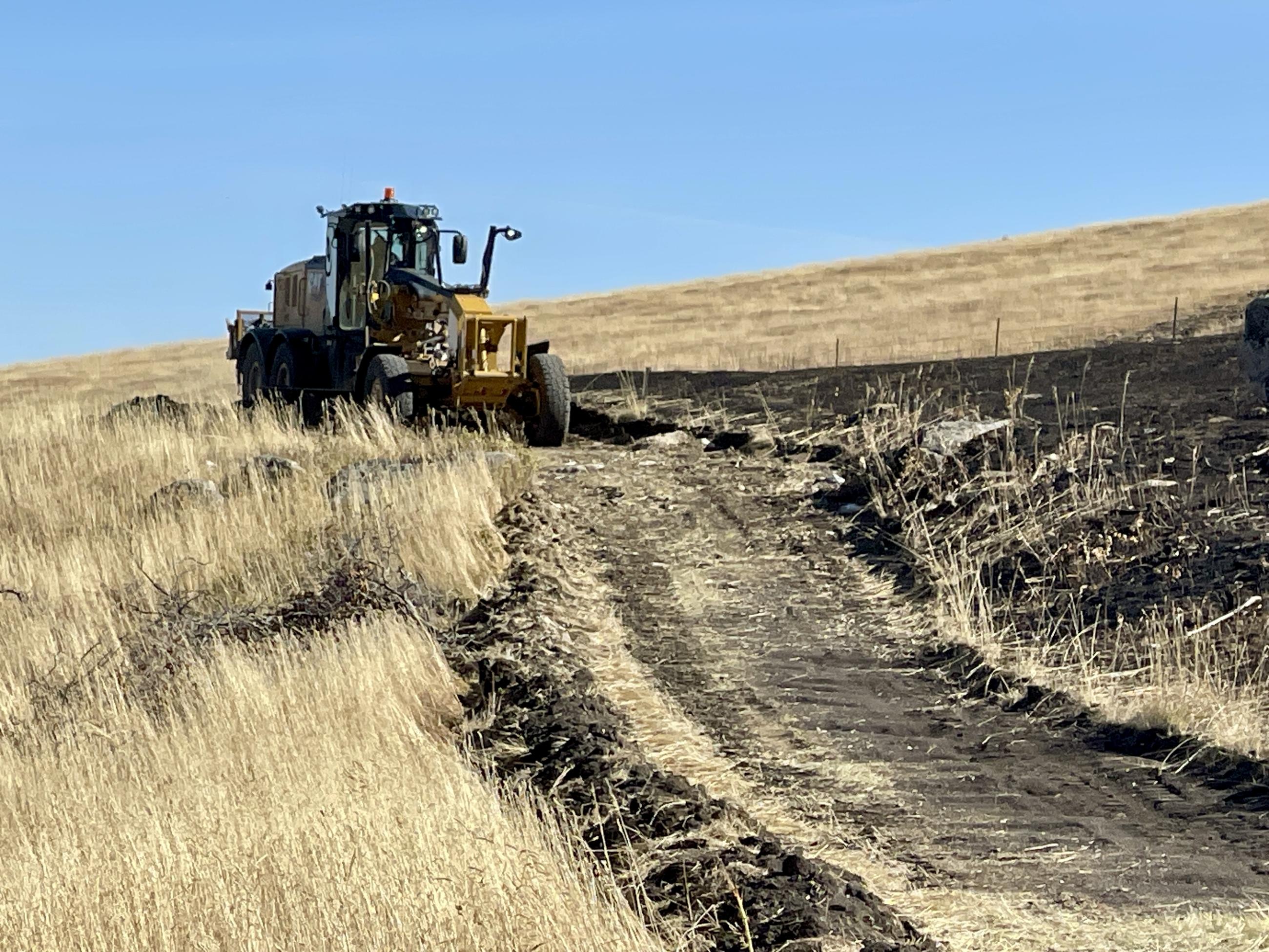 A road grader repairs and levels a bulldozed fireline before leaving the incident