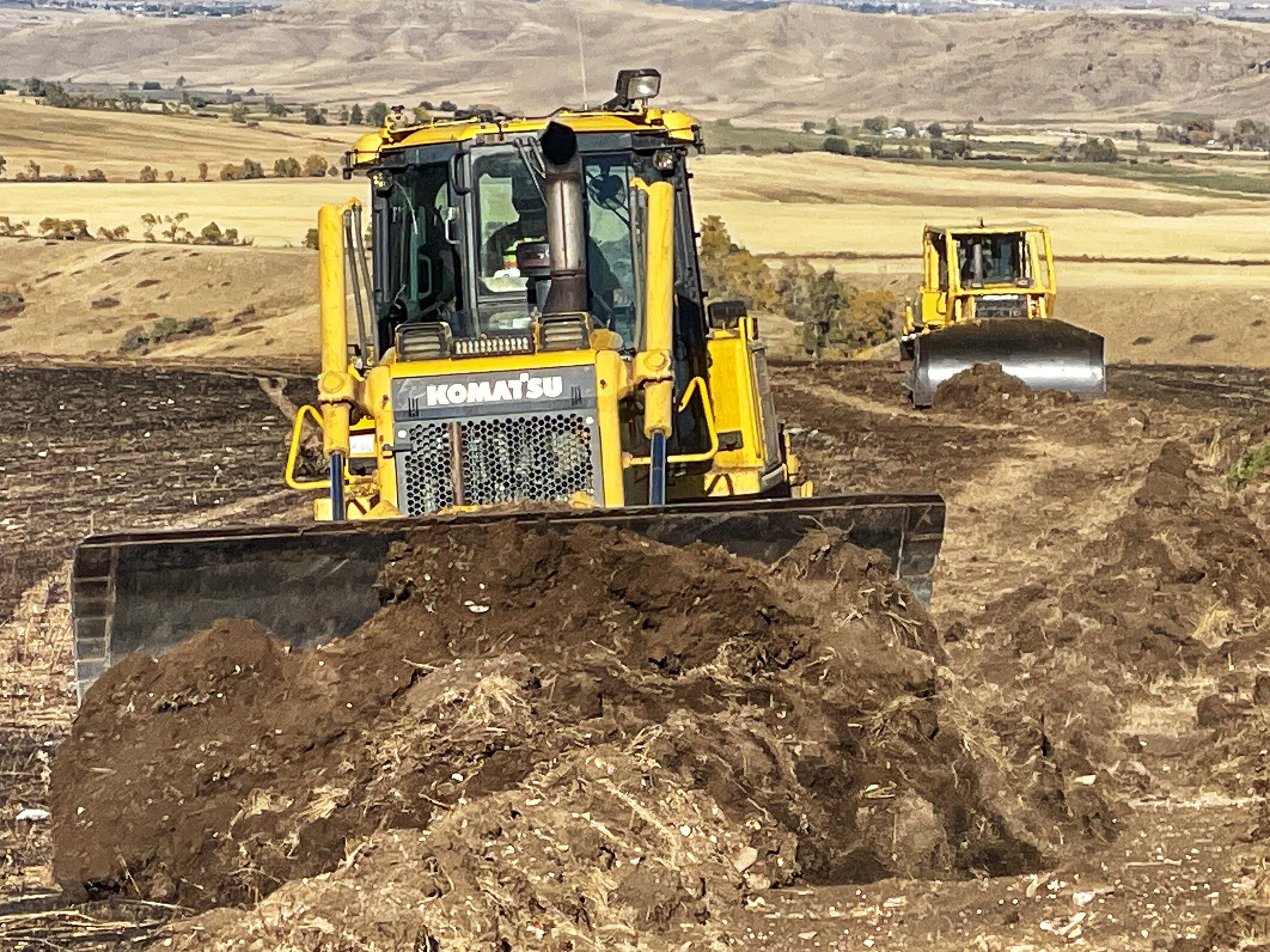 two bulldozers push berms of soil to level firelines