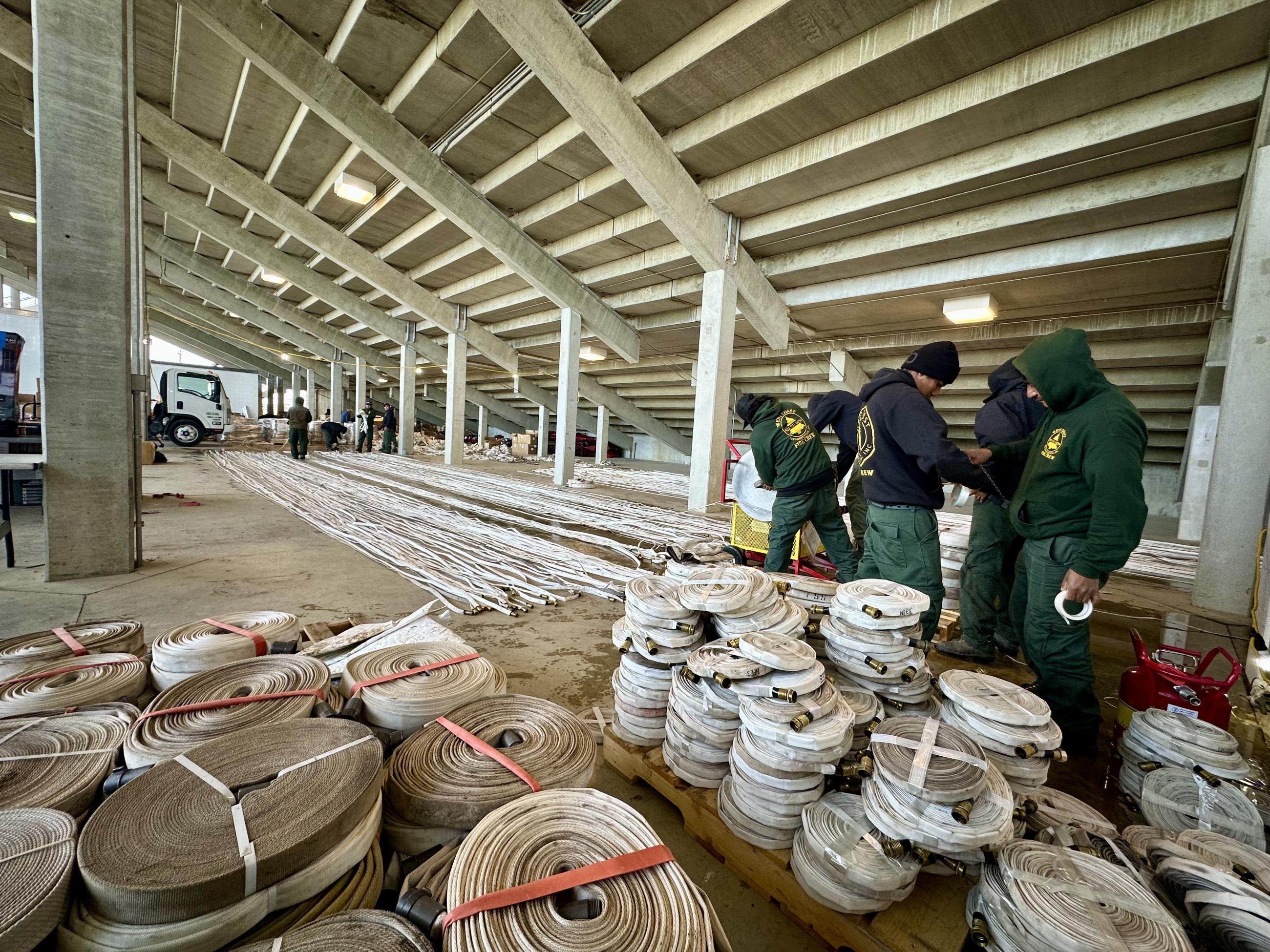 Workers stand among a large amount of rolled and stretched fire hose