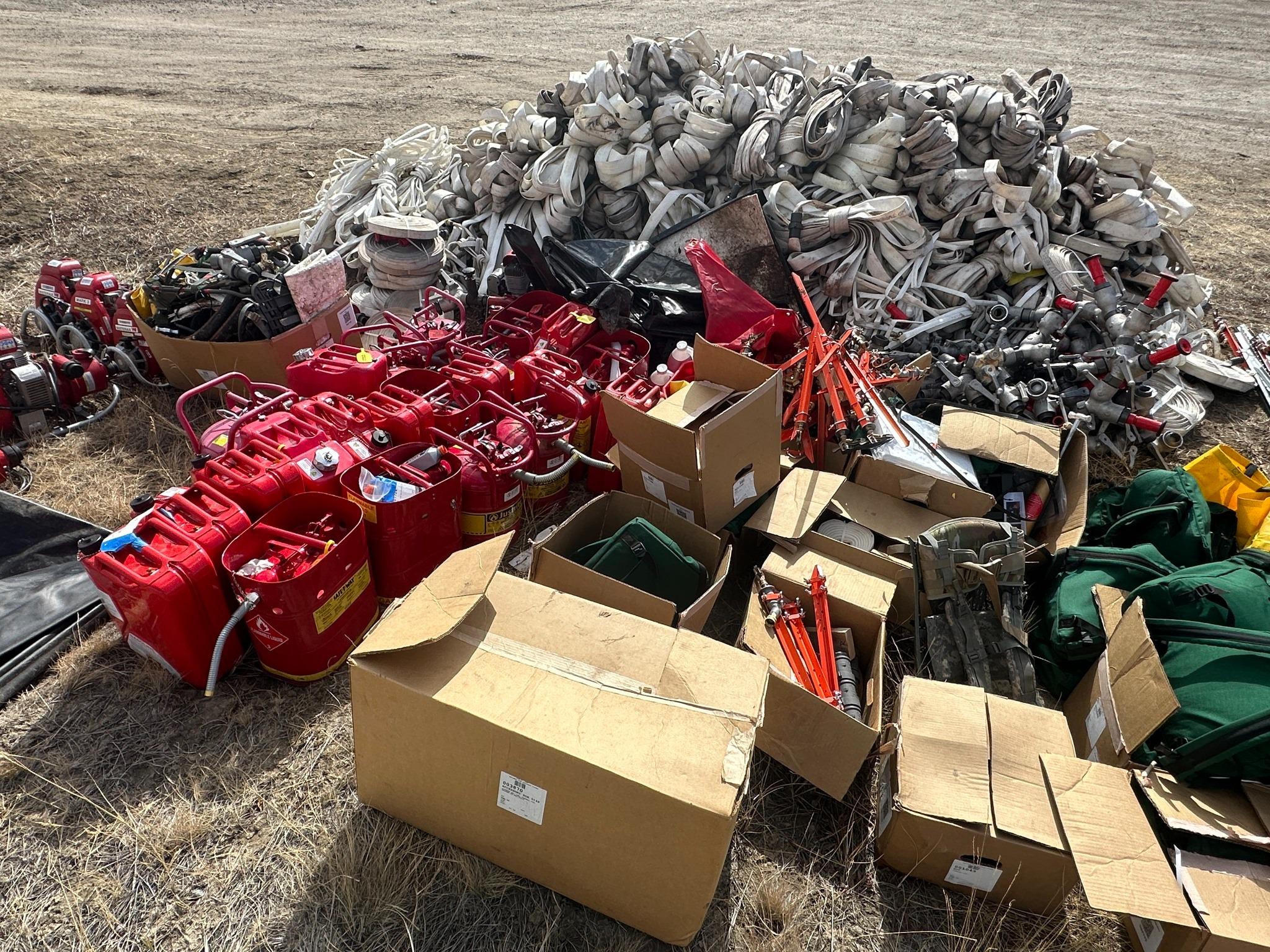 A file of empty fuel cans, cubes and fire hose sit on the dormant/brown  grass. 