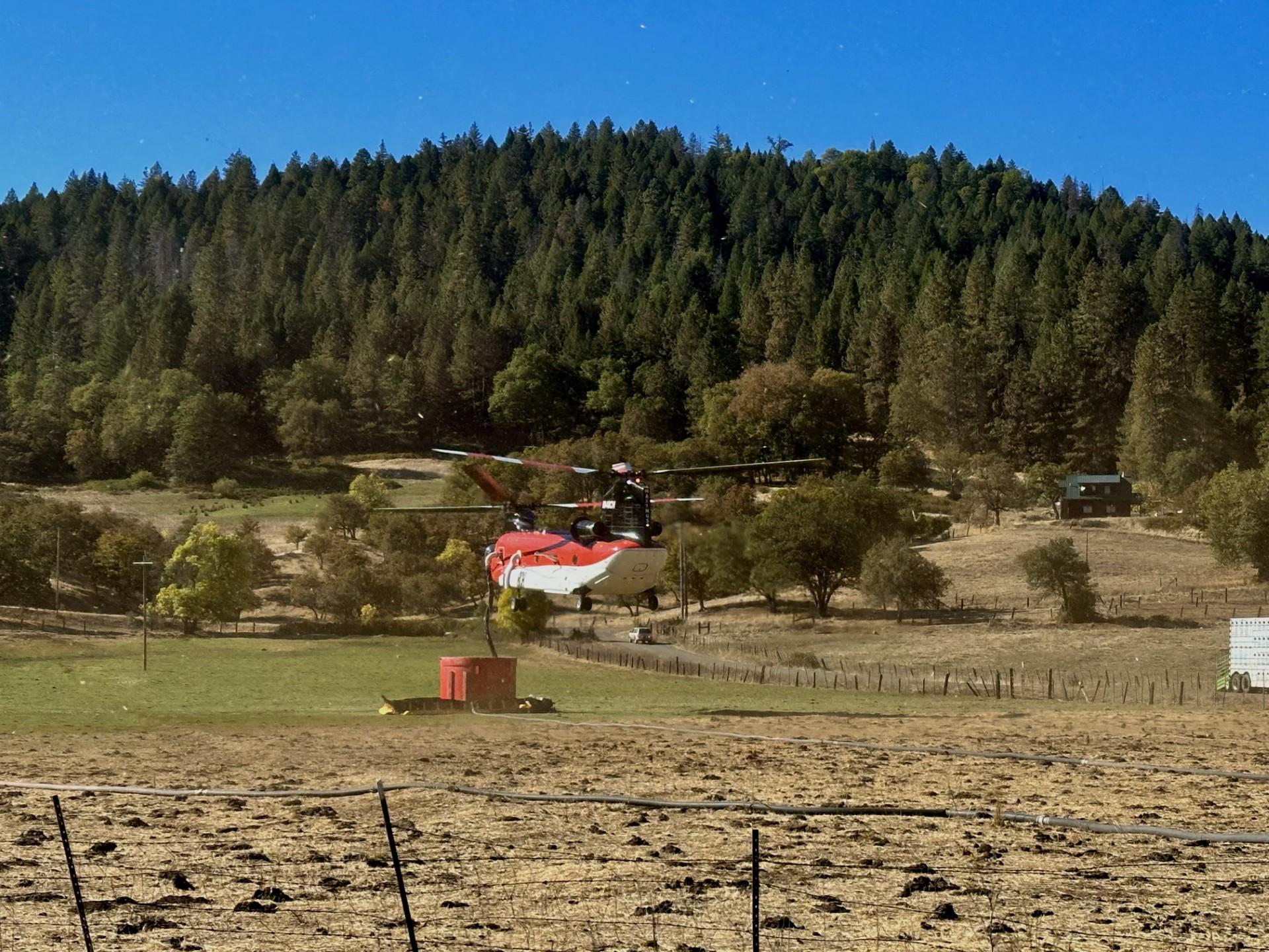 image of a red helicopter hovering over a tank in an open meadow.