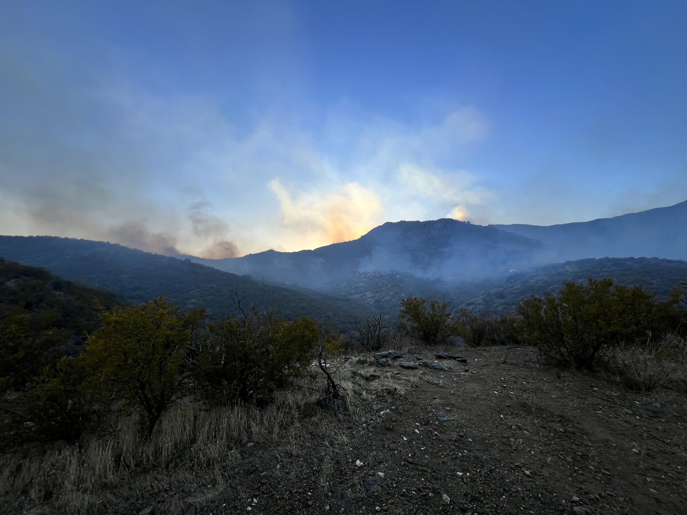 the sun shines from behind mountains through smoke