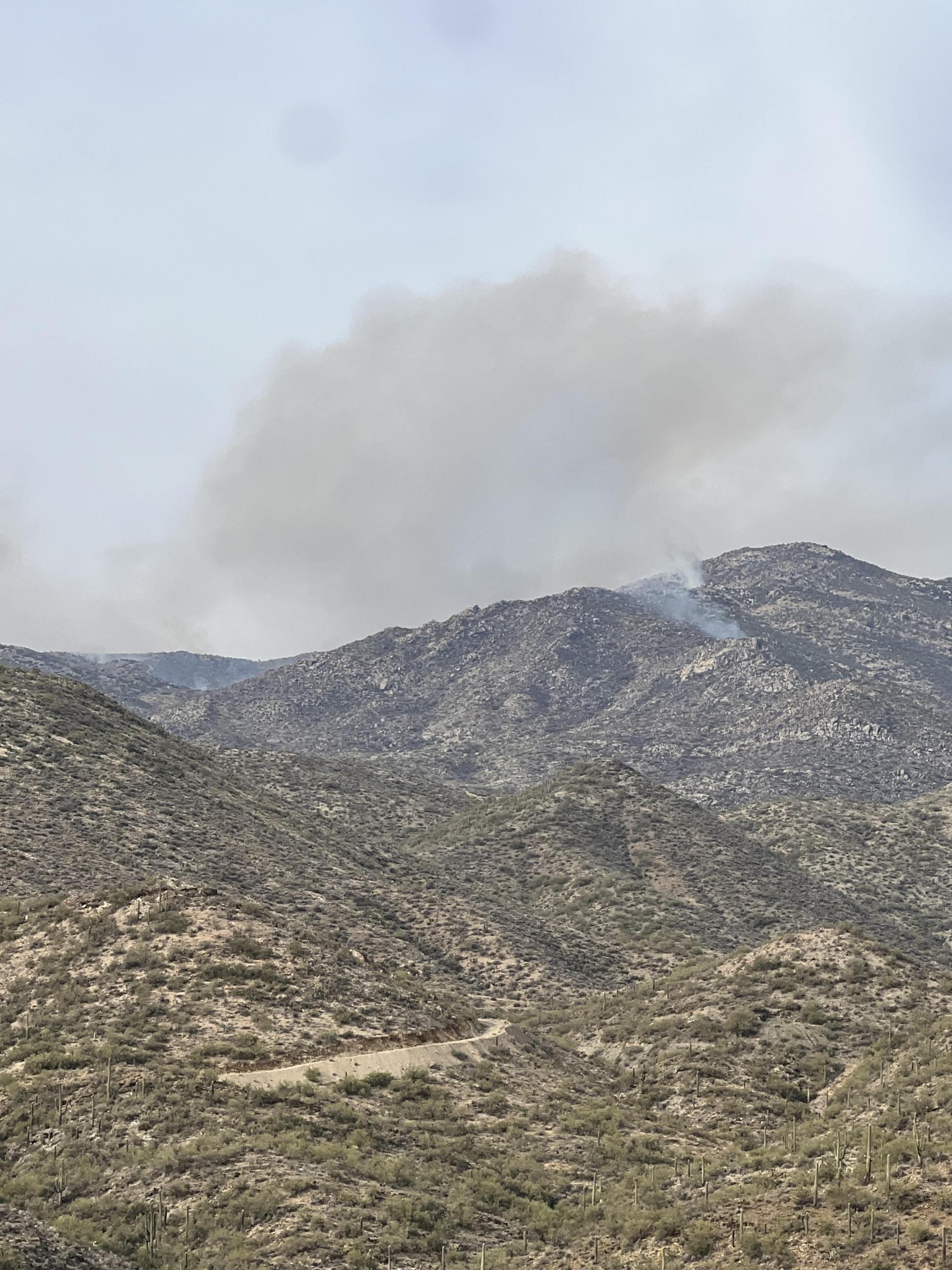 in a mountainous desert landscape, a smoke plume is visible