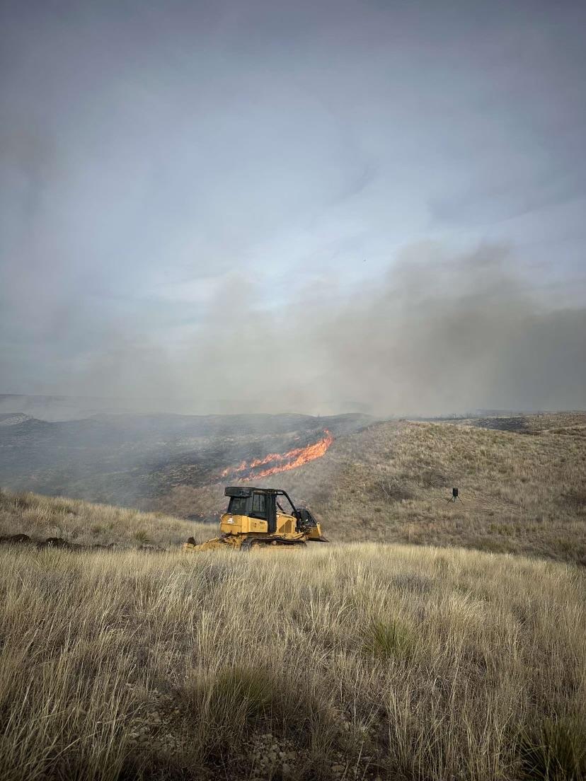 Texas A&M Forest Service Bull dozer creating fire breaks along the fire edge using a plow. Tall and thick grass fuel loading present in this image.