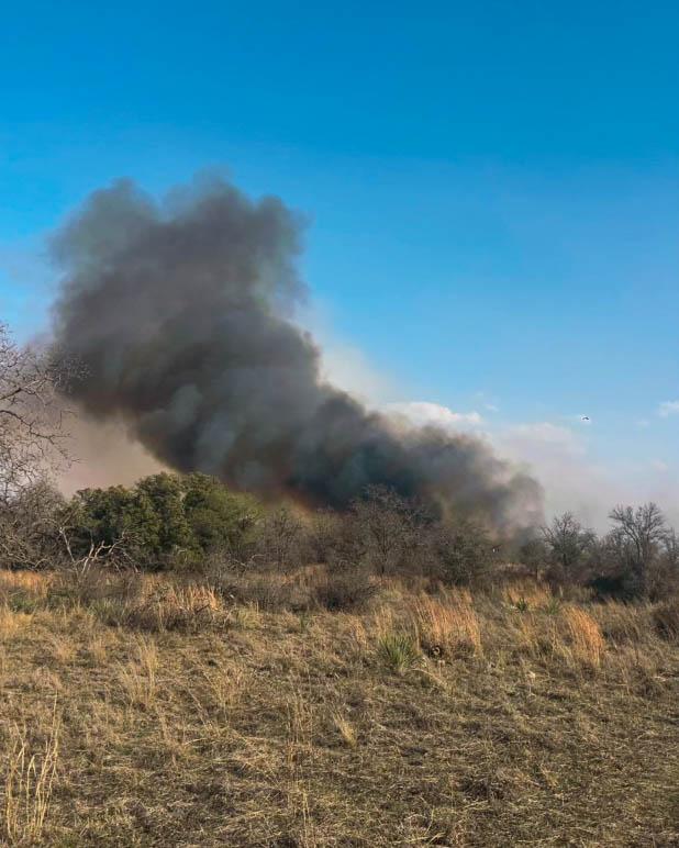 Dark smoke rising from brush, blue sky background