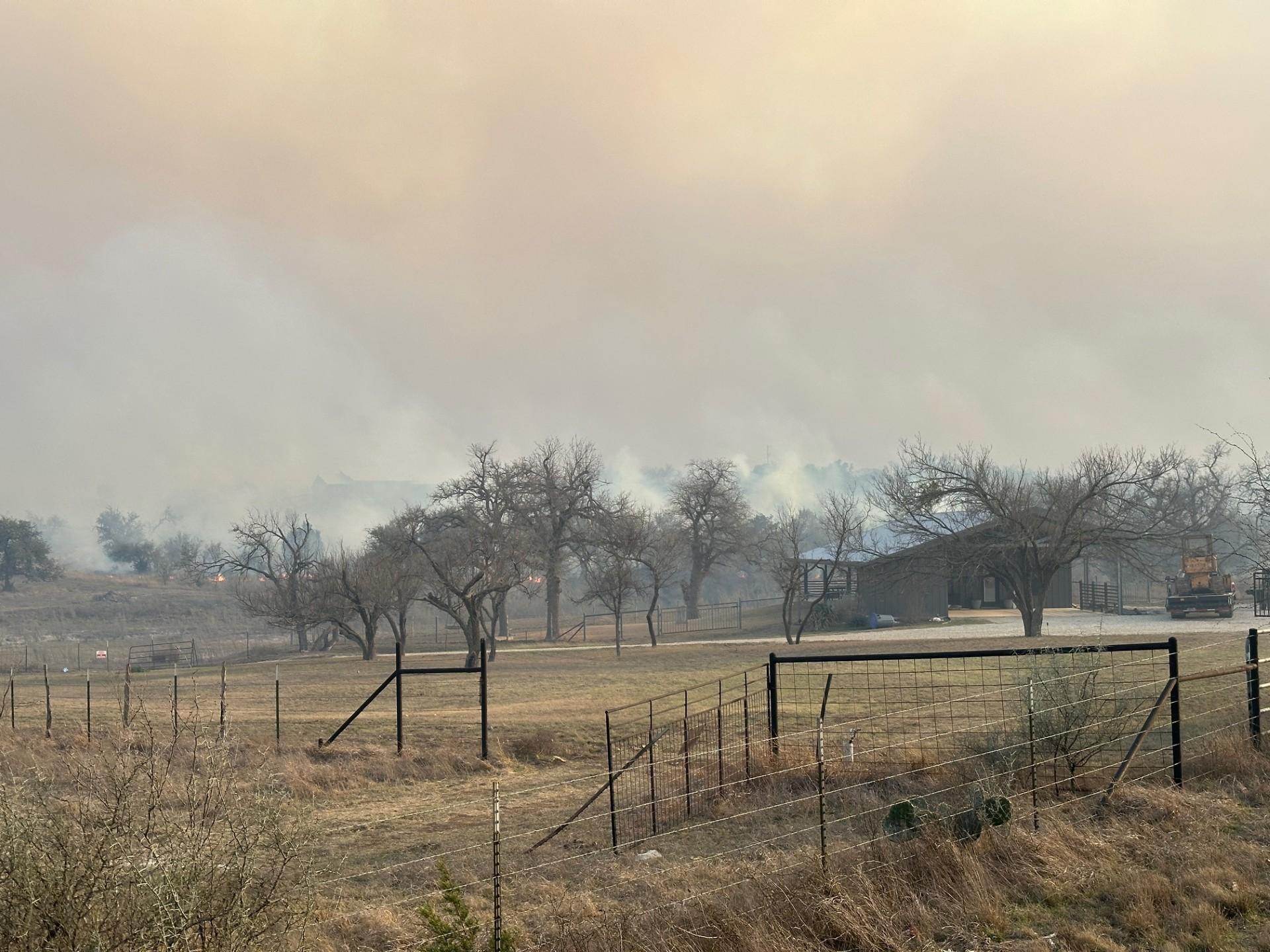 Fluffy smoke fills the upper half of the photo with trees and a grassy pasture below.