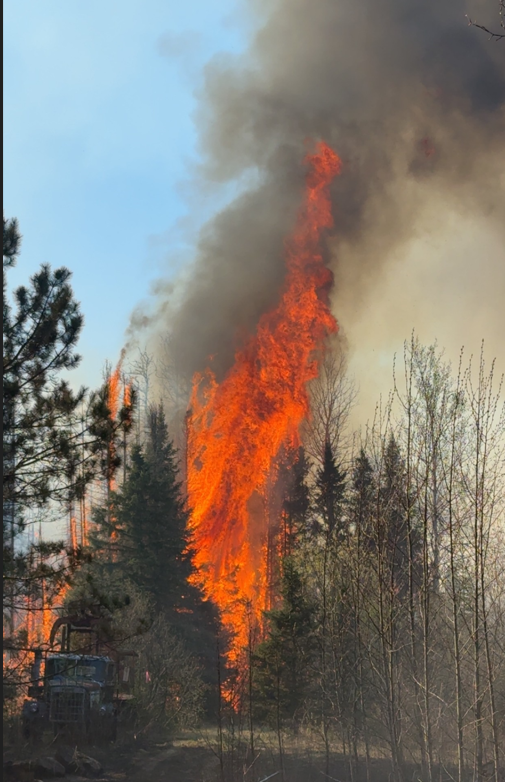 Large fire flame rising from a fire with a nearby old logging truck 