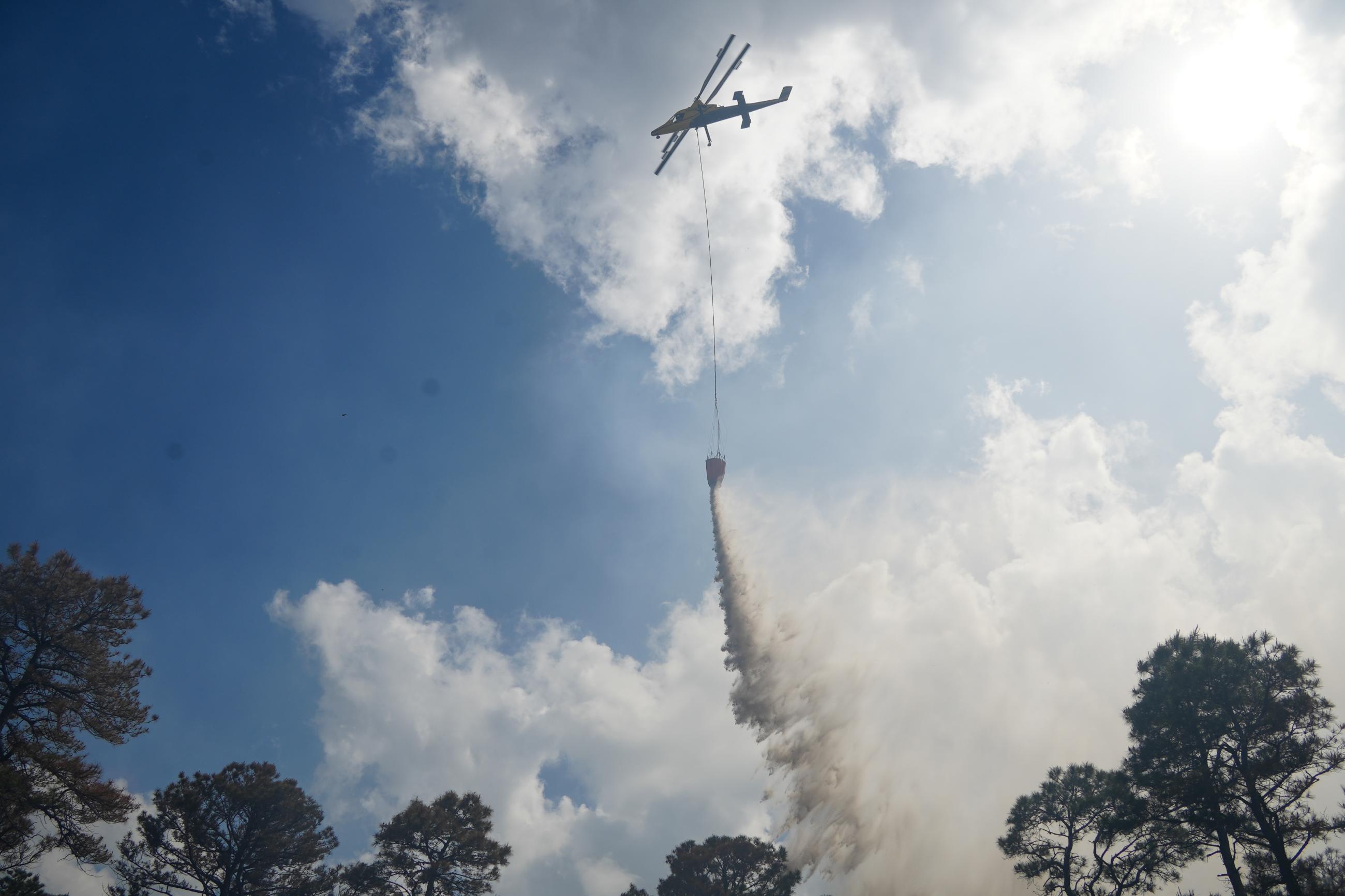 Helicopter drops water with trees in the background 