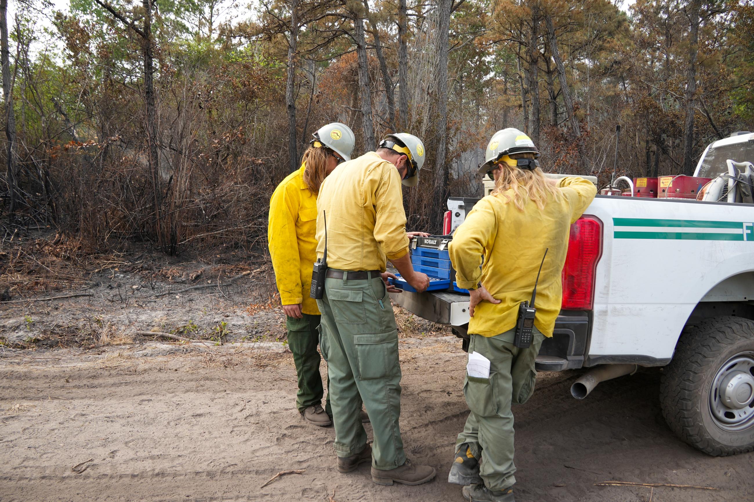 Firefighters gathered around truck bed, using tools to fix a water pump