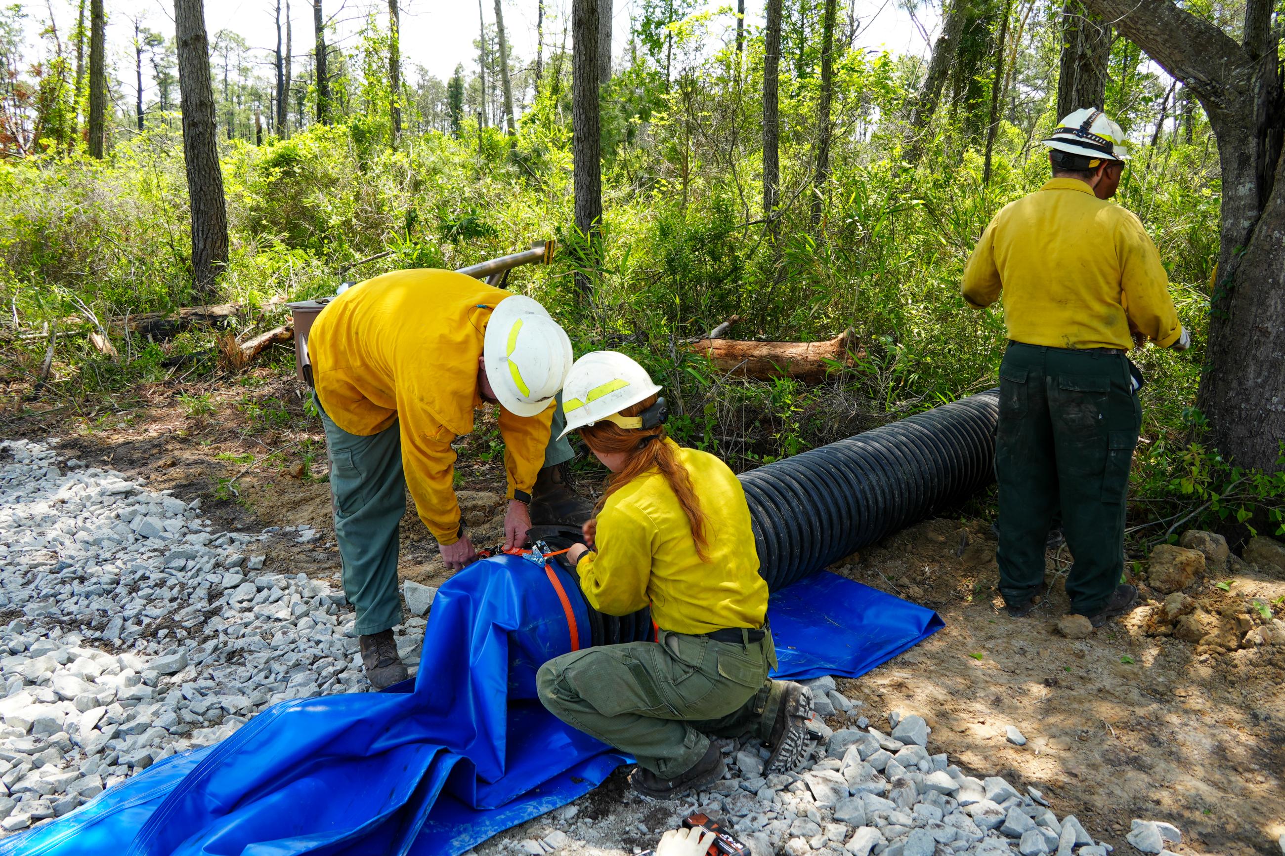 Three firefighters work to install a pump