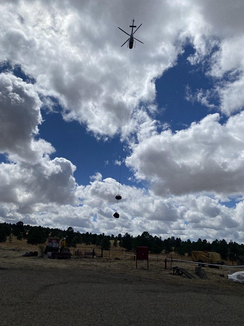 Helicopter with long line and gear hanging at the end against a cloudy blue sky