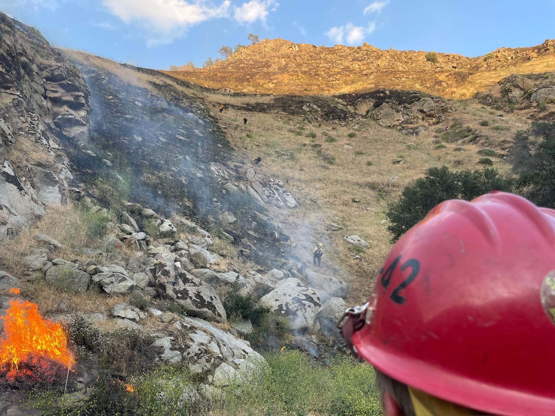 Firefighters hiking steep terrain to construct containment line.
