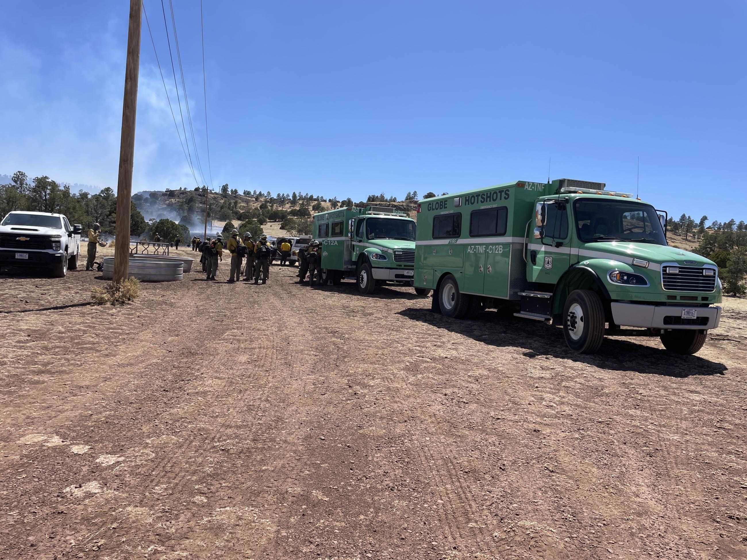 Large green trucks in a dirt parking lot. 