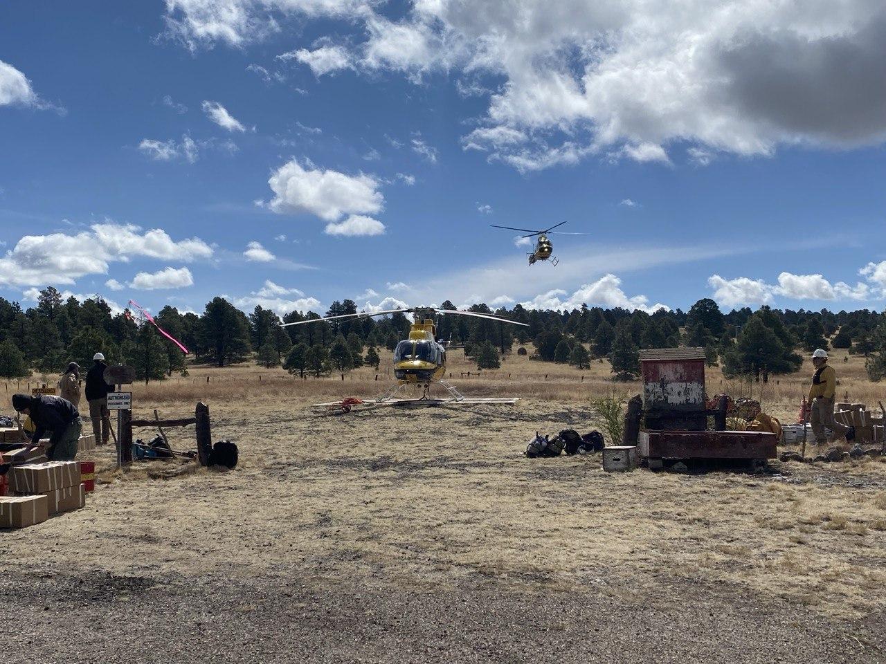 One helicopter on the ground and another coming in for a landing against a cloudy, blue sky
