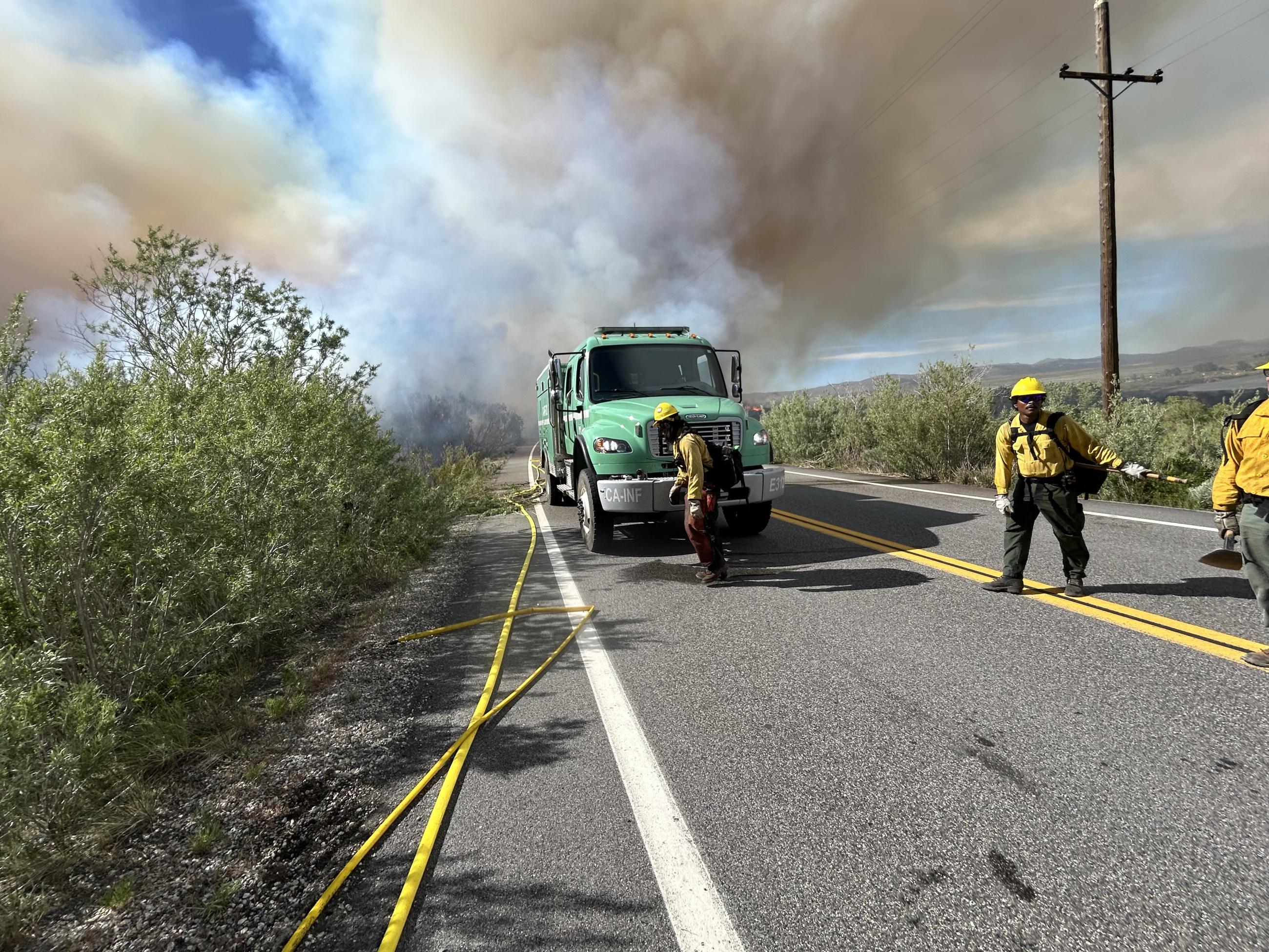 firefighters, green fire engine, hose, on highway, power lines, smoke, brush