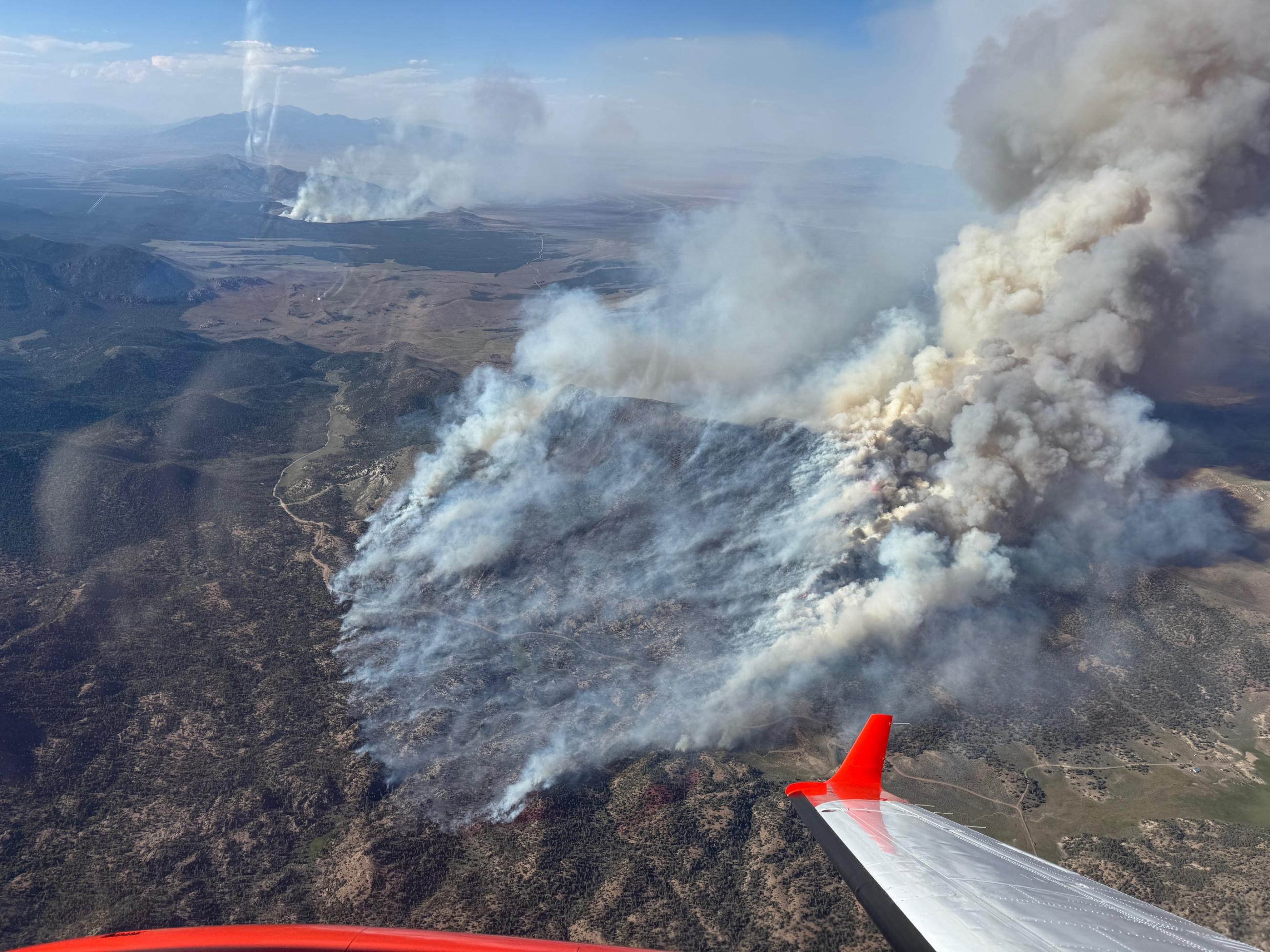 Aerial view from an airplane of mountainous terrain burning in two different places.