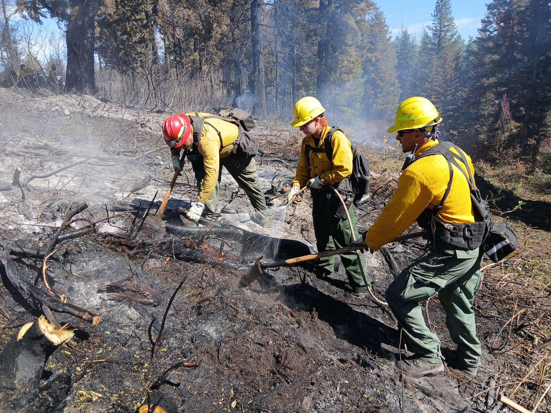 Three firefighter work with tools in a blackened area to ensure hot spots are out